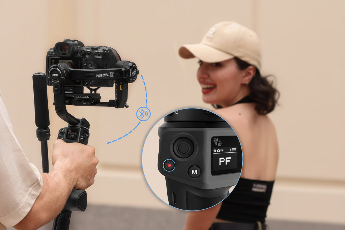Camera stabilizer with close-up of control panel held by a person, with a woman in the background.